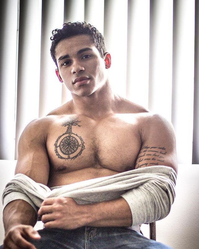 Noah Gray-Cabey showing his tattoo in a grey t-shirt and blue jeans.